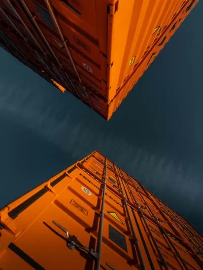Two bright orange shipping containers stacked high, photographed from below against a dark blue sky