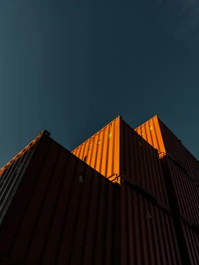 Stacked shipping containers, lit orange by low sun, against a deep blue sky