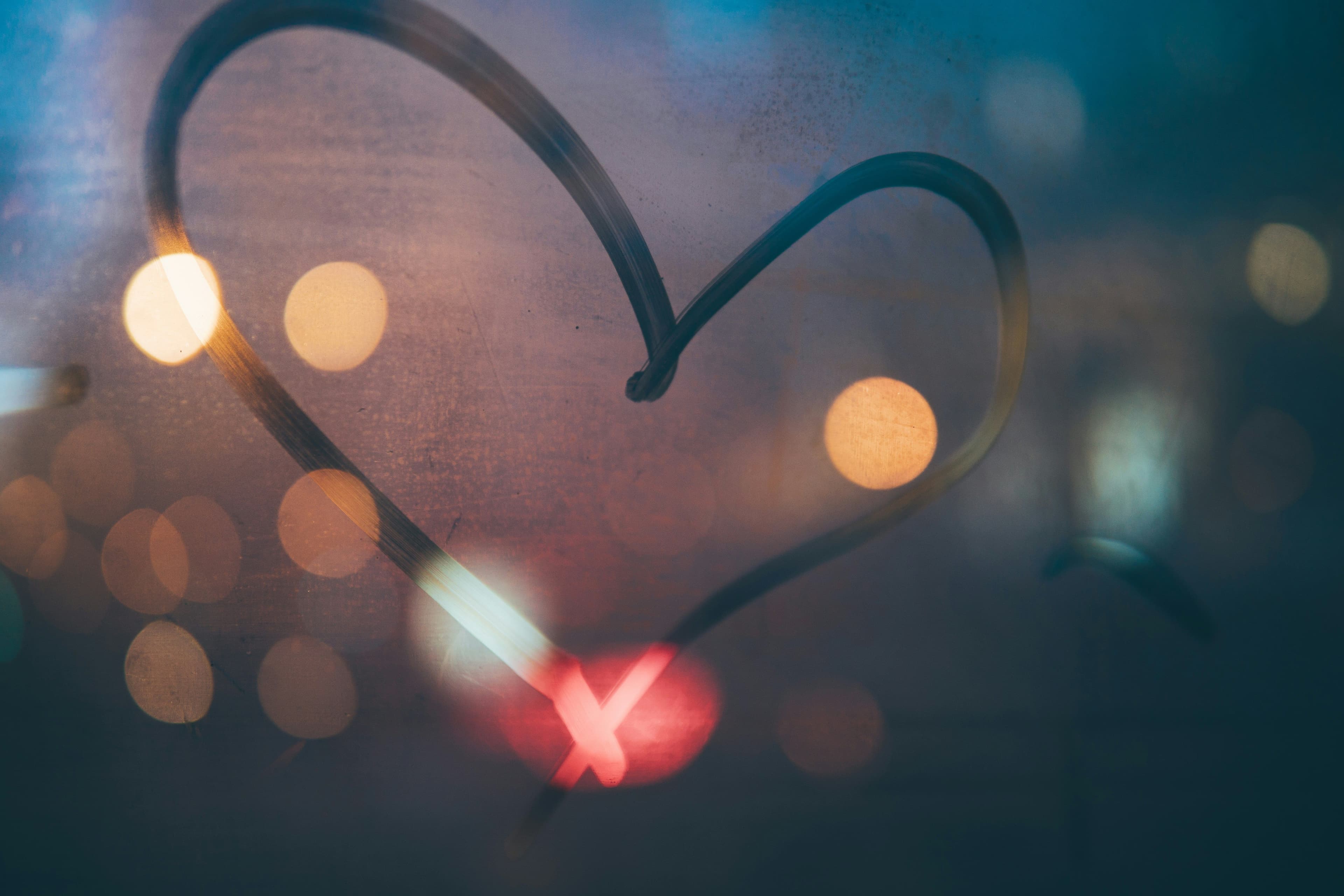 a heart is drawn on a window with lights in the background .