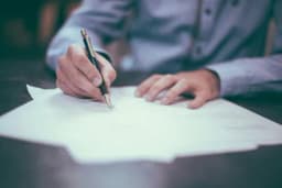 a man is writing on a piece of paper with a pen .