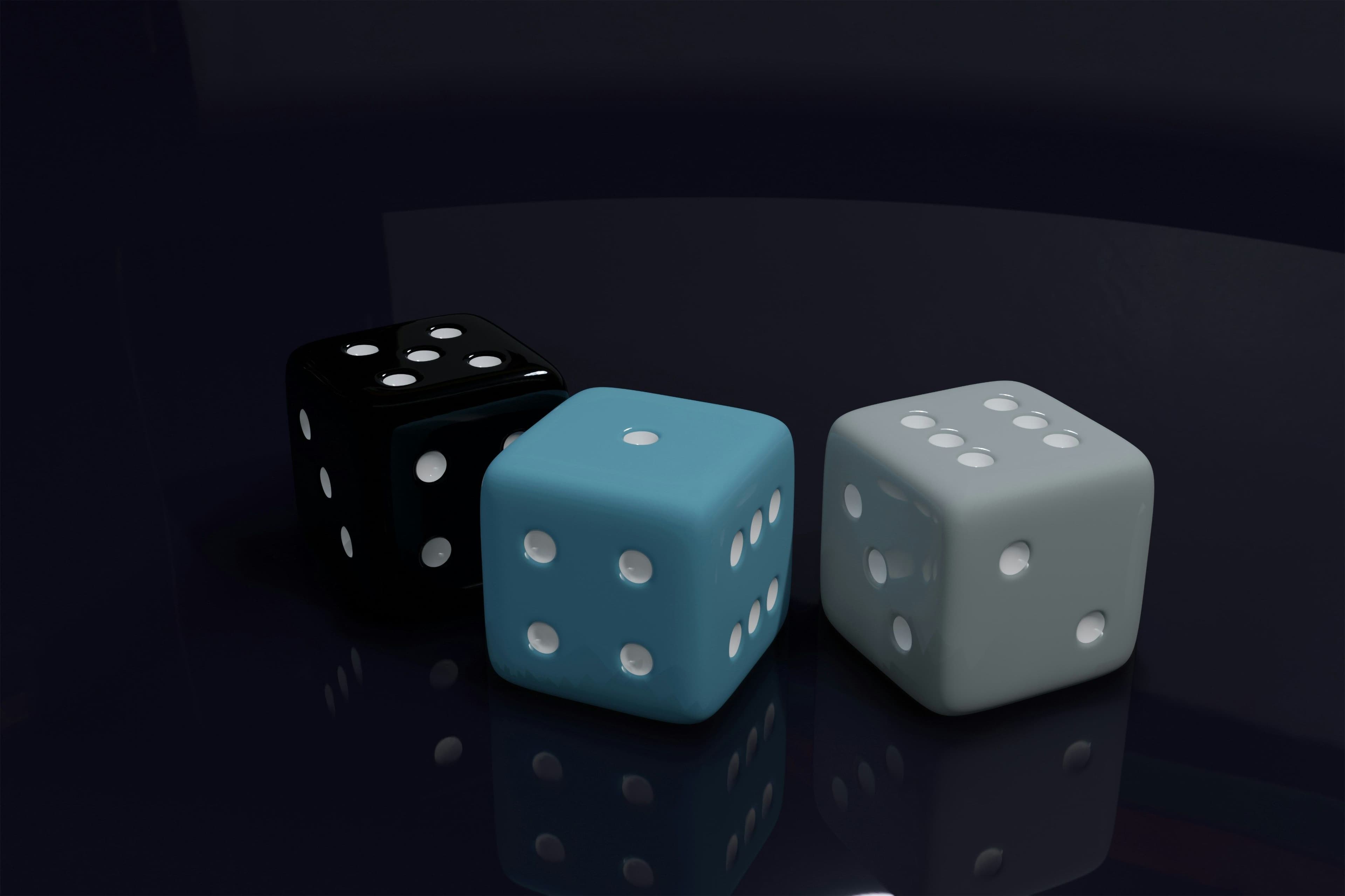 Three rendered dice on a dark reflective surface: black, teal and light grey, showing different pip counts