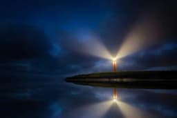 A lighthouse beaming light across the night sky, mirrored in still water below