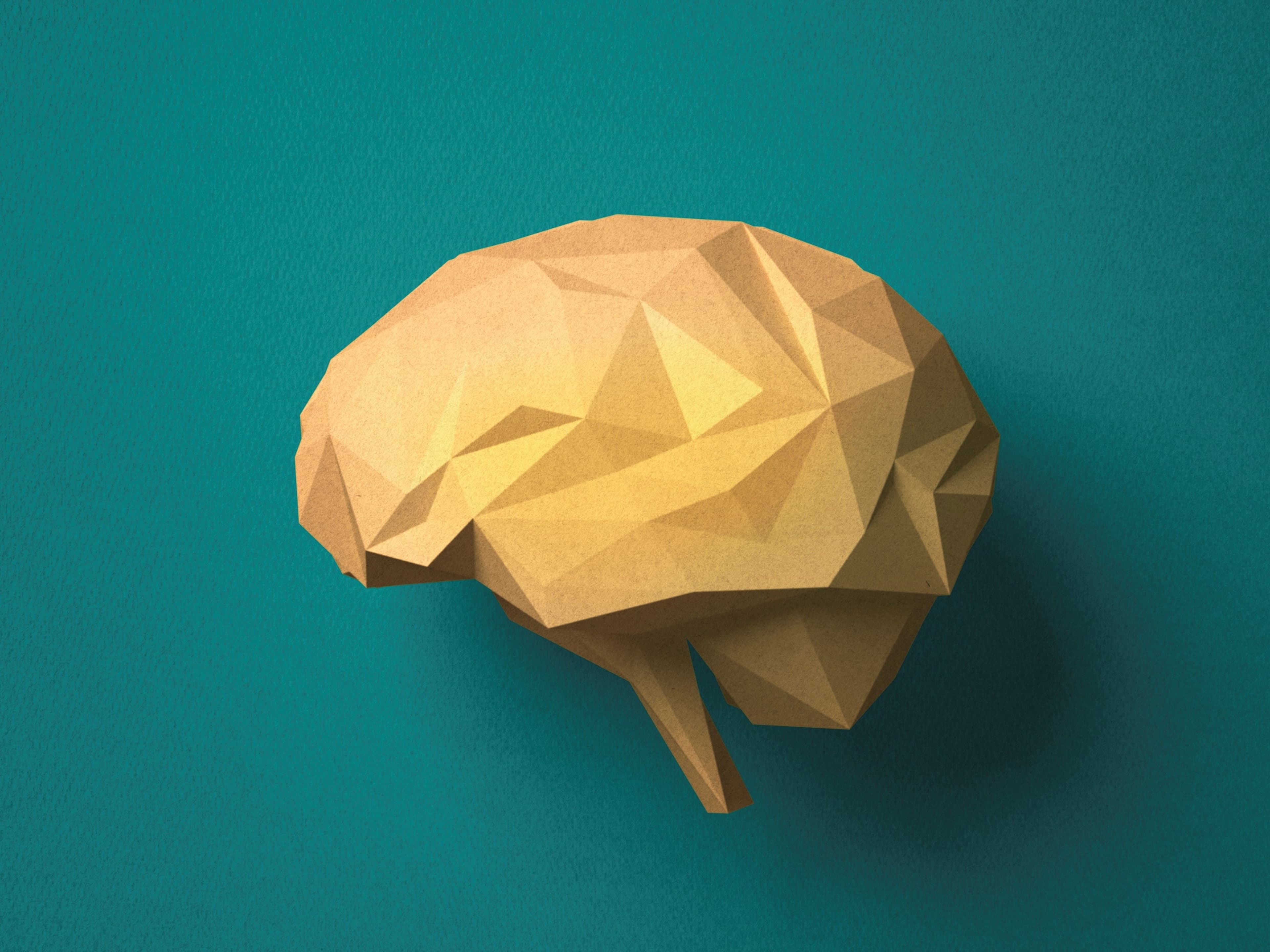 A low-poly, faceted paper model of a human brain in tan card on a teal background